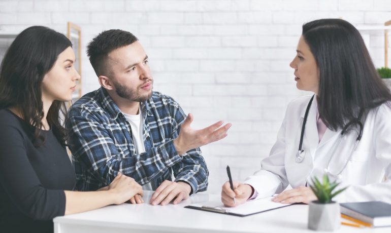 Young childless couple consulting with doctor at clinic